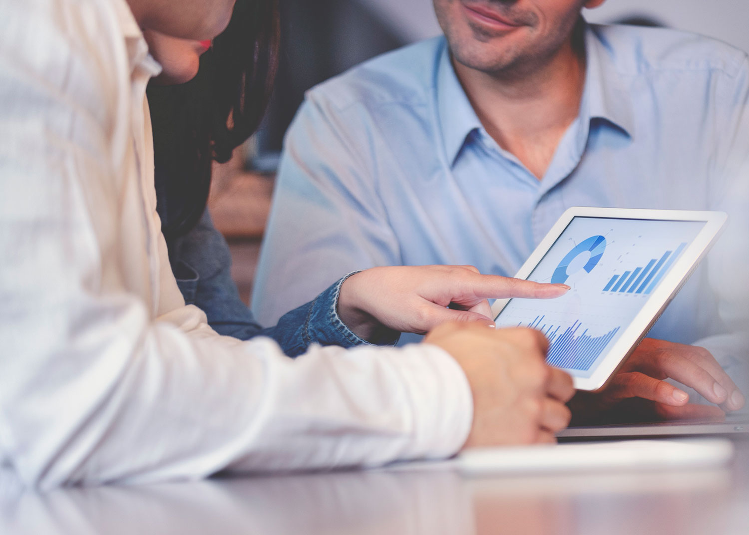 Three people from Fairway Partners examine a tablet displaying graphs and charts during a business meeting. A person points to data on the screen.